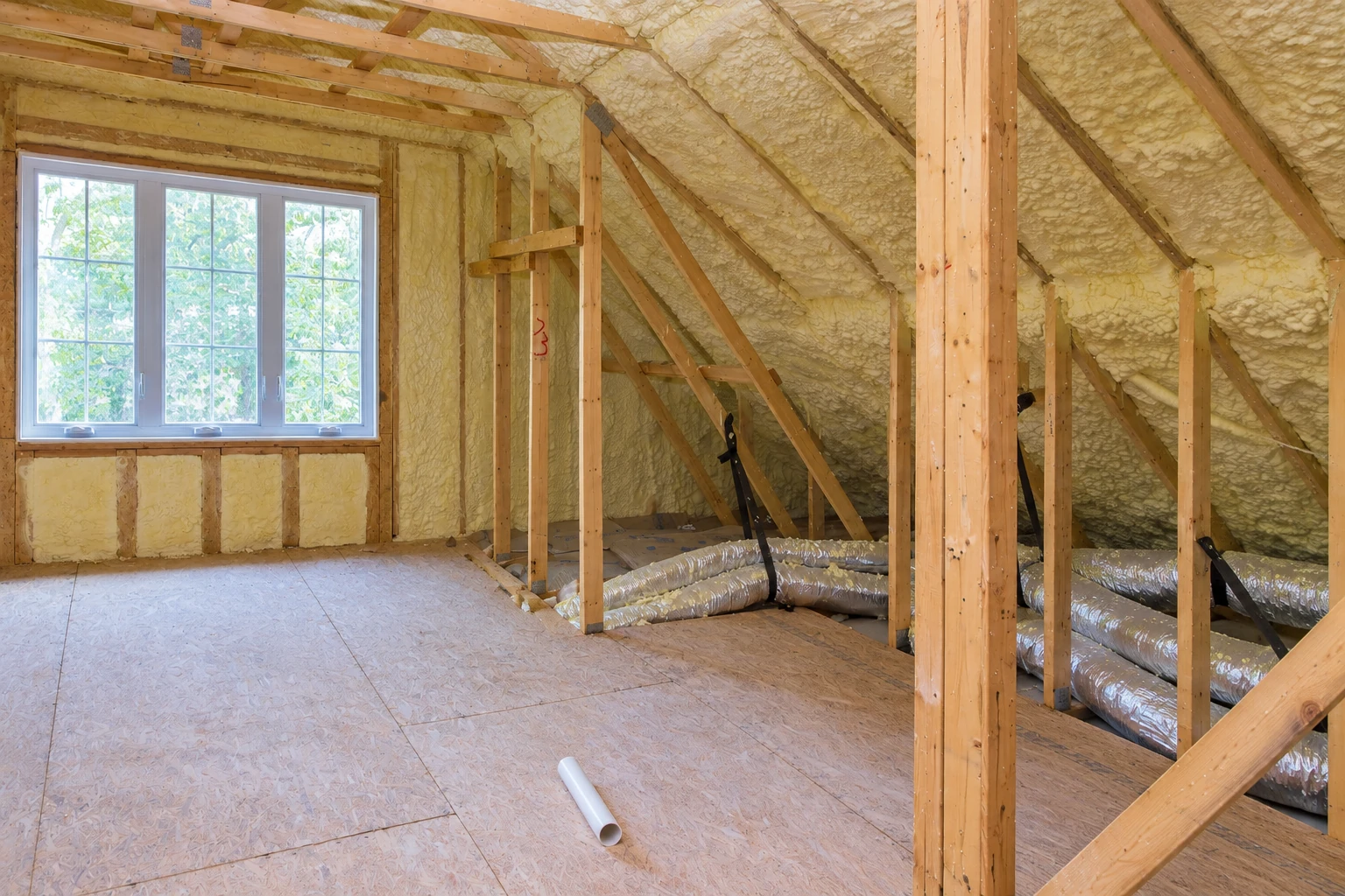 Attic with spray foam coating the roof and walls, exposed framing, and flexible ducts running across the floor.
