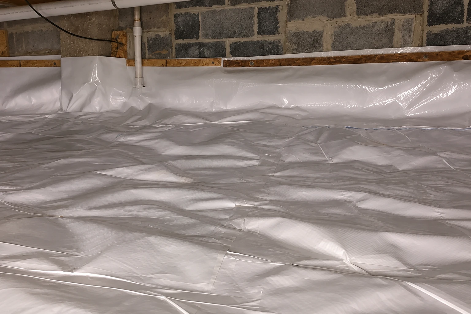 Crawl space floor and lower stone walls covered with a wrinkled white vapor barrier.