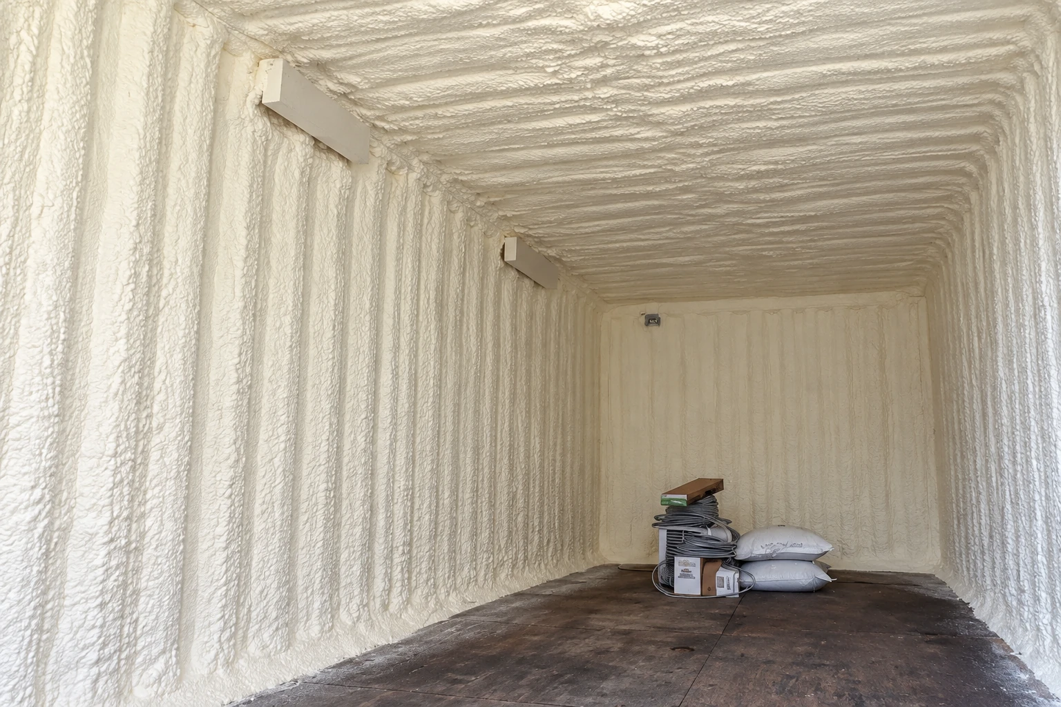 A room is enclosed in thick white spray foam across its walls and ceiling, with supplies stacked at the back.